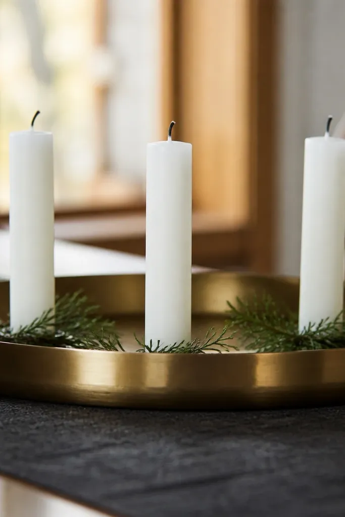 Brass tray with frosted white taper candles and a few green stems
